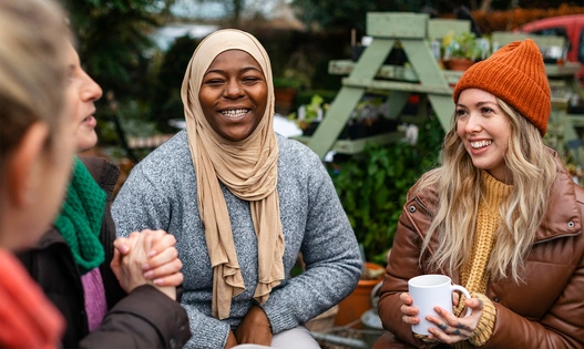 Group of warm clothed women, seated outside, smiling and laughing