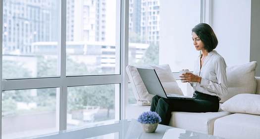 Une personne regarde son ordinateur, assise sur un fauteuil dans une pièce lumineuse